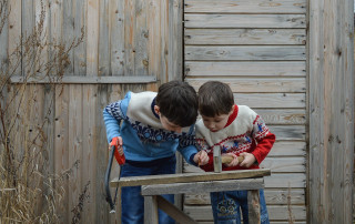 Zwei konzentriert arbeitende Kinder, etwa 8 Jahre alt, mit Säge und Hammer über ein Stück Holz gebeugt.