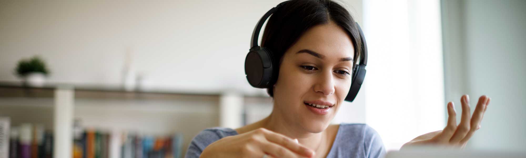 Junge Frau im Online‑Coaching mit Kopfhörern vor dem Laptop