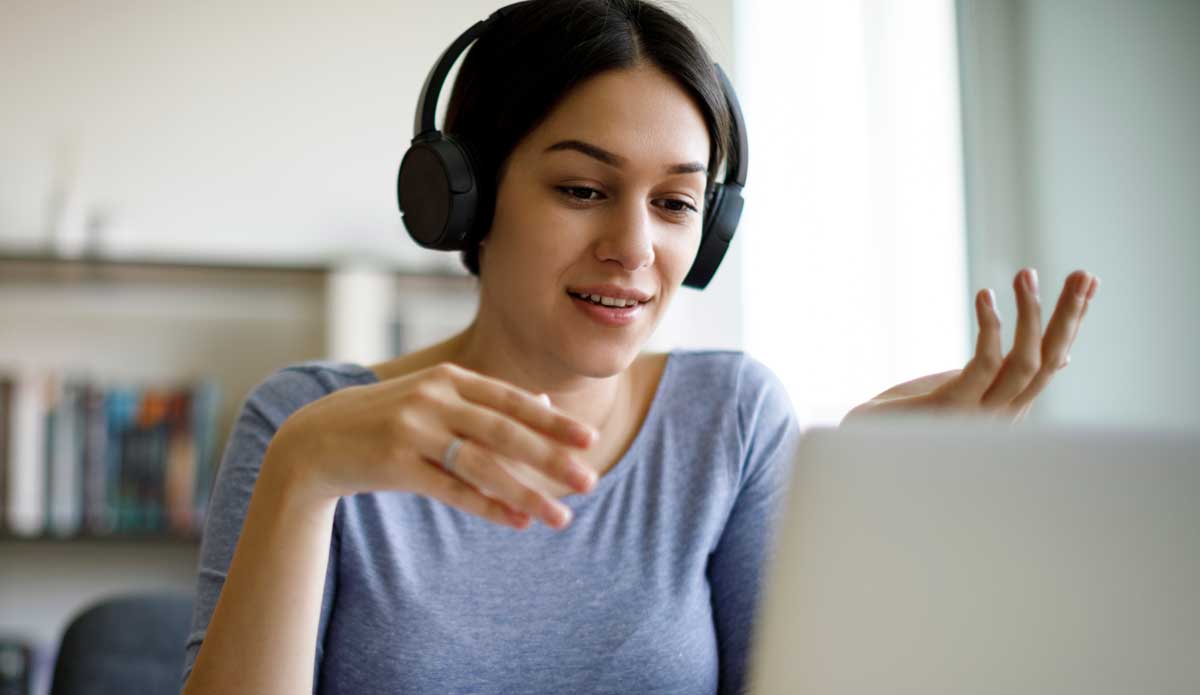 Junge Frau im Online‑Coaching mit Kopfhörern vor dem Laptop